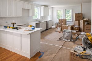 Interior photograph of a kitchen renovation in progress in a Philadelphia suburban home, showing a mix of completed and in-progress work: new white shaker cabinets partially installed, quartz countertops being fitted, stainless steel appliances in boxes, hardwood floors protected with paper, natural light from large windows, professional contractor tools visible but organized, before-and-after transformation feeling. Editorial renovation photography style, bright and airy, showing the process of improvement.